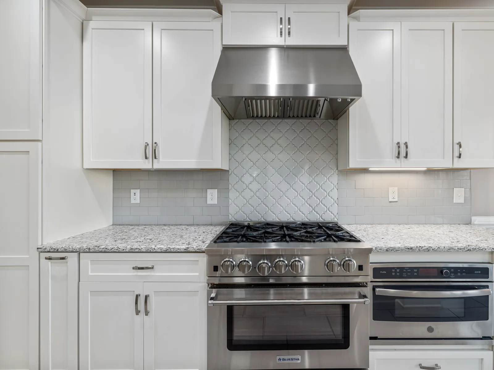 Stainless steel gas range under a vent hood in a white kitchen